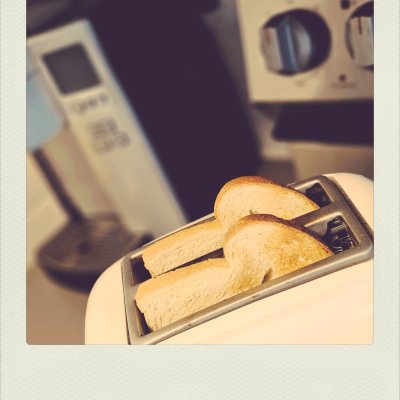 High-angle shot of two slices of bread in a toaster with a blurred kitchen background in warm tones.