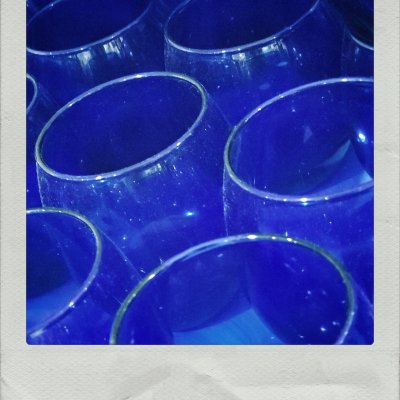 A close-up, high-angle view of several round, deep blue glass cups or bowls clustered together. The glass has a slightly dusty texture with soft light reflections along the rims and curved surfaces, creating a rich monochromatic pattern within a white instant-photo frame.