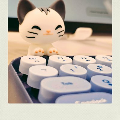 A close-up of a small white cat figurine with a smiling expression, resting its paws on the edge of a keyboard. The keyboard has round, light-blue keycaps with labels like 'ESC', 'Tab', and 'F1'. The background is softly blurred.