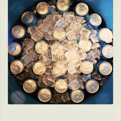 A top-down view of a blue round container packed with square ice cubes and blue aluminum beverage cans arranged in a circle.